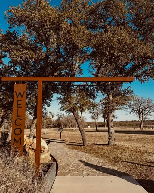 The rust-red Welcome gate at Lost Draw's vineyard, framed by live oaks