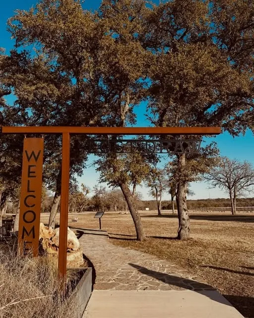 The rust-red Welcome gate at Lost Draw's vineyard, framed by live oaks
