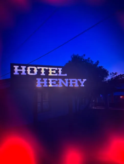 The Hotel Henry's neon sign glowing against a blue-hour sky in Blanco, Texas