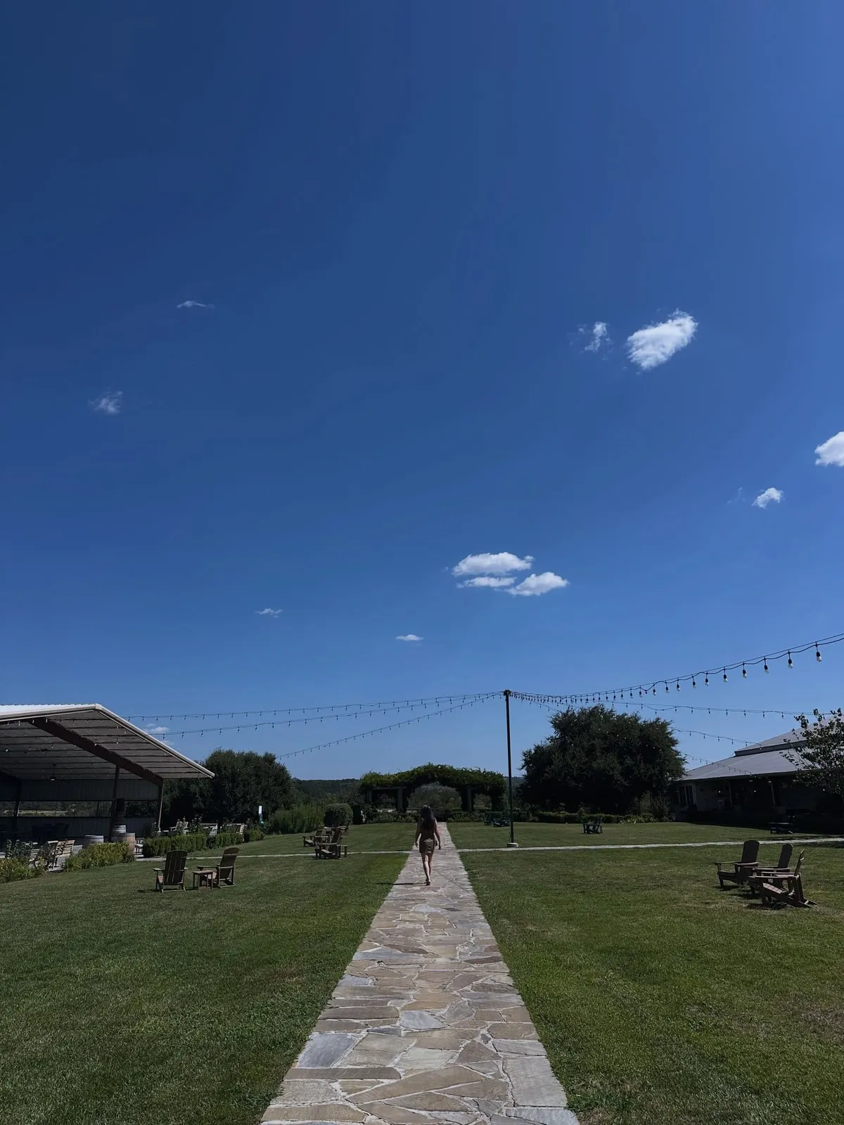 A flagstone path across the lawn toward the pavilion, string lights overhead and Hill Country sky