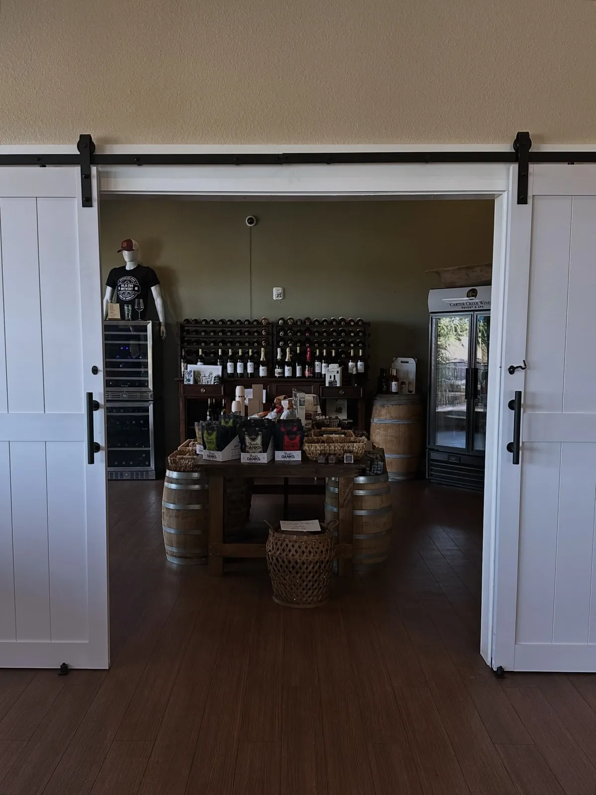 Barn doors sliding open on the Carter Creek tasting room — wine bottles, barrels and a tasting table