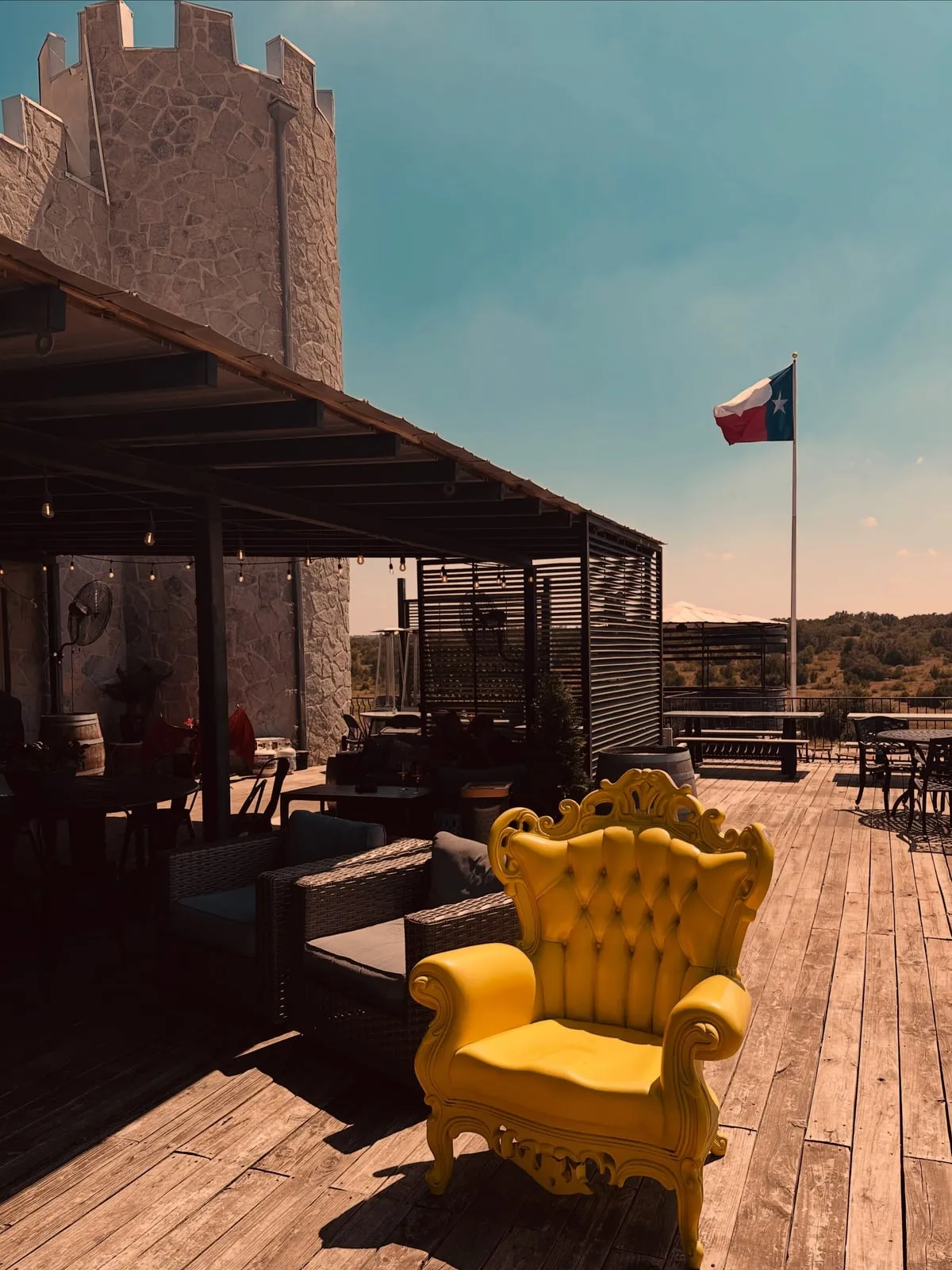 A castle turret above a covered wooden patio at Republic Wine Castle, a yellow throne chair in the sun and the Texas flag flying